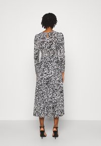 Zwart-witte jurk met een bloemenpatroon, lange mouwen, een sleutelgat achter en een vloeiende middellange rok, gecombineerd met zwarte hoge hakken sandalen.