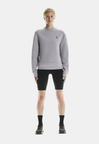 Un sweat-shirt lilas avec un col rond, des poignets côtelés et des détails de logo ; associé à un short de vélo noir et des chaussures de sport noires.