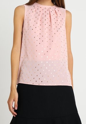 Sleeveless light pink blouse with metallic gold square dots, round neckline with soft pleats, worn with a black skirt.