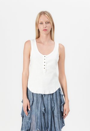 Witte geribde tanktop met een ronde halslijn, voorzien van vijf knopen aan de voorkant en een licht gebogen zoom. Gecombineerd met een blauwe rok met ruches.
