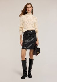 Pletený krémový svetr s texturovaným vzorem, černá sukně z umělé kůže se zipy a pásem, černé vysoké boty do kolen a malá kabelka.