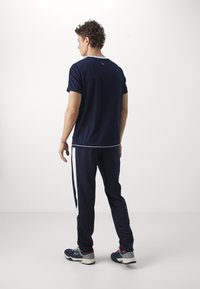 Navy Sportanzug bestehend aus einem kurzärmligen Shirt und einer Hose mit weißen Seitenstreifen. Das Shirt hat einen Rundhalsausschnitt und eine glatte Textur.