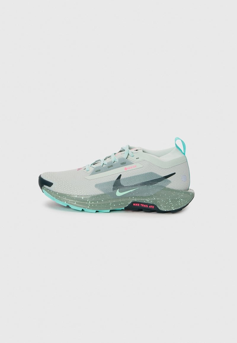 Chaussure de trail running Nike gris clair avec des touches bleu clair, logos noirs et roses, semelle texturée et languette au talon.