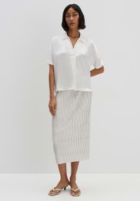 Blusa bianca a maniche corte con colletto abbinata a una gonna midi con linee verticali grigio chiaro. Sandali con un leggero tacco.