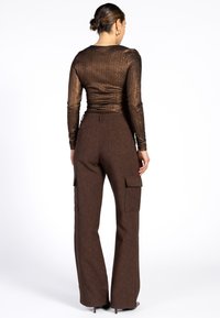 Bruine, gestructureerde cargobroek met zijzakken en een getailleerde, metallic bronzen top met lange mouwen, gezien vanaf de achterkant.
