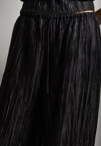 Pantalones negros de pierna ancha y plisados con cintura elástica y cordón, que exhiben una textura arrugada y un diseño fluido.