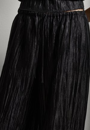 Pantaloni neri a pieghe, con gamba larga, cintura elastica e cordoncino, che presentano una texture a righe e un design fluido.