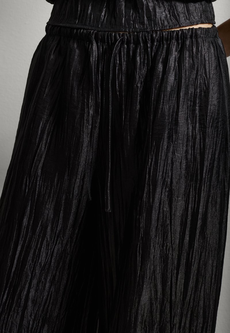 Pantalones negros de pierna ancha y plisados con cintura elástica y cordón, que exhiben una textura arrugada y un diseño fluido.