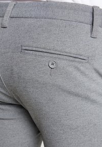 Szare dopasowane spodnie o gładkiej fakturze, z pojedynczą tylną kieszenią zapinaną na szary guzik oraz płaskim pasem.