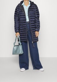 Laivaston sininen toppatakki hupulla, vaaleansininen pikeepaita, tummat leveälahkeiset farkut ja pieni teksturoitu turkoosi käsilaukku. Valkoiset tennarit täydentävät asun.