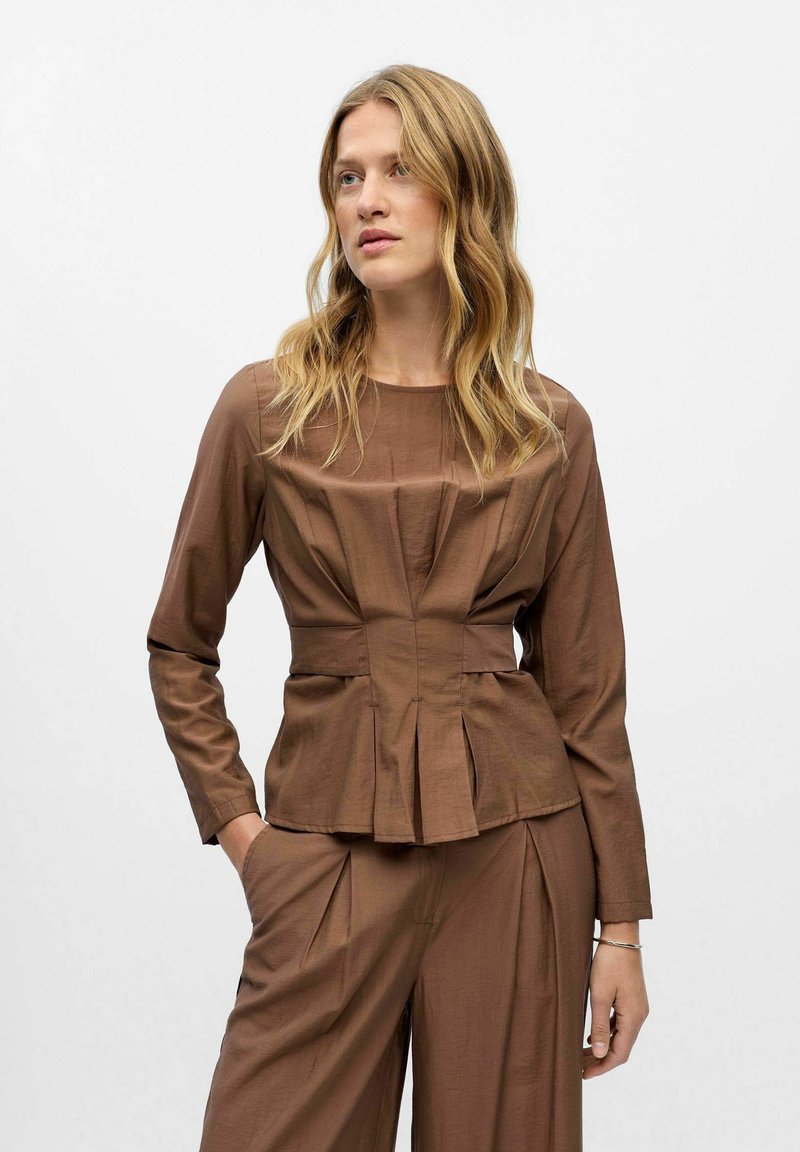 Brown, fitted top with long sleeves and a pleated design. Features a round neckline and a tailored silhouette with a peplum effect.