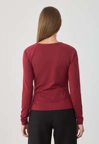 Burgundi színű, hosszú ujjas felső, puha anyagból készült. Kerek nyakkivágással és testhezálló fazonnal rendelkezik, raglán ujjakkal.