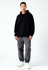 Felpa nera con cappuccio e tasca frontale, abbinata a pantaloni cargo grigi con tasche laterali e polsini elasticizzati, indossata con sneakers bianche.