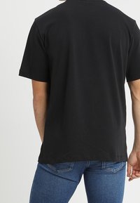 Czarny bawełniany T-shirt z krótkimi rękawami i okrągłym dekoltem. Gładka faktura, prosty krój, brak widocznych wzorów lub zdobień na plecach.