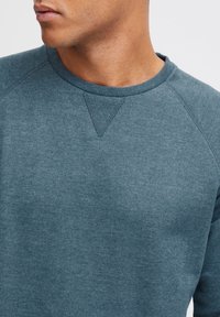 Sudadera de color teal oscuro hecha de una mezcla de algodón, con un cuello redondo, mangas raglán y acentos de punto texturizado en los hombros.