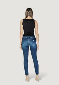 Camiseta sin mangas negra y jeans ajustados azul oscuro. Los jeans cuentan con bolsillos traseros y acentos de costura clara. Modelo lleva tacones beige.