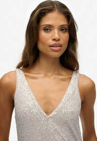 Silberner Paillettenoberteil mit tiefem V-Ausschnitt, schmalen Trägern und glatter Textur, die das Licht reflektiert und einen schimmernden Effekt erzeugt.