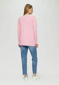 Lichtroze langwerpige trui met een ronde halslijn, ontspannen pasvorm en zijsplitten, gecombineerd met lichtblauwe jeans en metallic sneakers.
