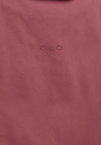 Tessuto rosa polvere con trama diagonale sottile e piccolo logo in rilievo "Khujo Co" al centro.