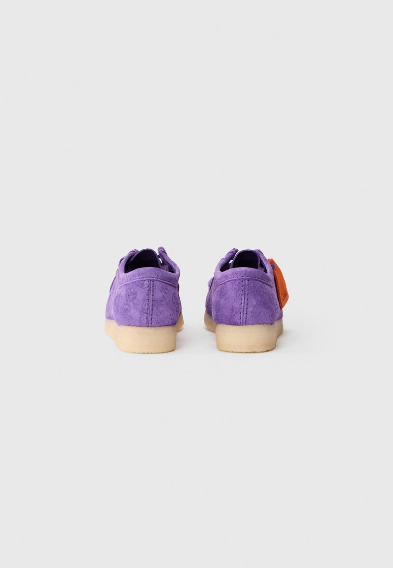 Chaussures en daim violet avec un motif texturé, dotées d'une semelle en caoutchouc légère et d'une étiquette orange sur la chaussure droite. Vue arrière.