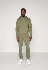 Conjunto de hoodie verde-oliva e calças a combinar, feito de algodão macio, com bolso frontal tipo canguru, cordões e punhos canelados.