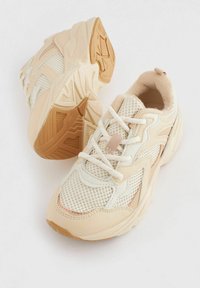 Beige und weiße Sportschuhe mit Netzpanelen, Gummisohlen, strukturierten Akzenten und Schnürsenkeln. Abgerundete Form und gepolsterter Innenraum für Komfort.
