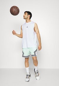 Biała sportowa koszulka bez rękawów z czarnym logo, miętowe szorty z czarnymi akcentami i białe buty sportowe. Koszykówka jest w powietrzu.