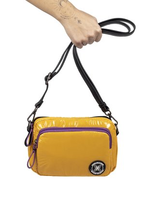 Gelbe Nylon-Umhängetasche mit glänzendem Finish, ausgestattet mit einer lila Reißverschlusstasche und einem schwarzen Ledergriff. Enthält ein rundes Logo-Detail.