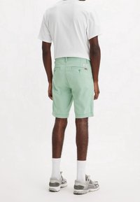 Miętowe szorty o prostym kroju, z dwiema tylniymi kieszeniami i podwiniętymi nogawkami. Połączone z gładką białą koszulką i szarymi butami sportowymi.