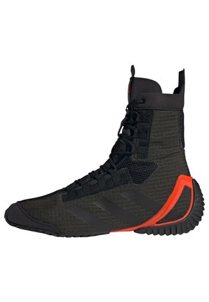 Chaussure de sport noire montante en tissu texturé, lacets noirs, design discret à trois bandes et accent rouge-orange sur le talon de la semelle.