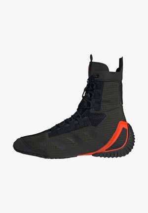 Chaussure de sport noire montante en tissu texturé, lacets noirs, design discret à trois bandes et accent rouge-orange sur le talon de la semelle.