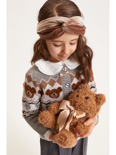 Cardigan gris tricoté avec un motif d'ours en peluche, col blanc et boutons argentés ; tenant un ours en peluche marron avec un ruban crème.