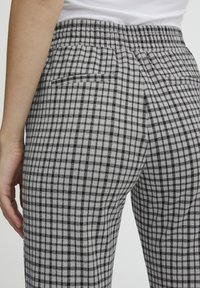 Czarno-białe spodnie w kratę o teksturowanym wykończeniu, z płaskim pasem i tylnymi kieszeniami, charakteryzujące się dopasowanym krojem i zwężającymi się nogawkami.