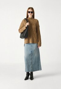 Camisola castanha de malha tricotada com gola alta, combinada com uma saia comprida de ganga. Mala preta para o ombro e botas de biqueira fina completam o conjunto.