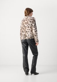 Pull en tricot avec imprimé léopard dans des nuances de beige et de marron, associé à un pantalon en cuir noir et des bottines à talons pointus.