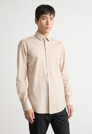 Ljust beige långärmad skjorta med ett subtilt mönster, knäppning vid kragen och manschetterna, tillverkad av ett mjukt, lätt tyg.