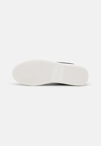 Semelle en caoutchouc blanche d’une basket avec un motif à chevrons en diamant et le nom de la marque Jack & Jones embossé au centre.