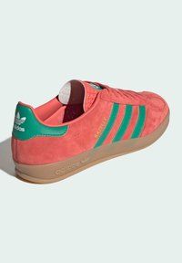 Ružové semišové tenisky so zelenými pruhmi, s gumovou podrážkou a vypolstrovaným golierom. Branding je viditeľný na jazyku a päte.