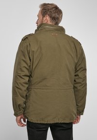 Olive green jacket with a high collar, zipper, and shoulder epaulets. Features a relaxed fit and soft fabric texture.