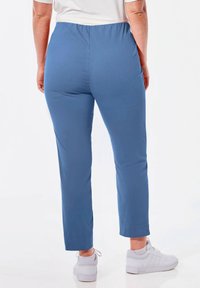 Blauwe stretchbroek met een elastische tailleband, smal gesneden en enkel-lang. Gedragen met witte sport sneakers. Glad stoftextuur.