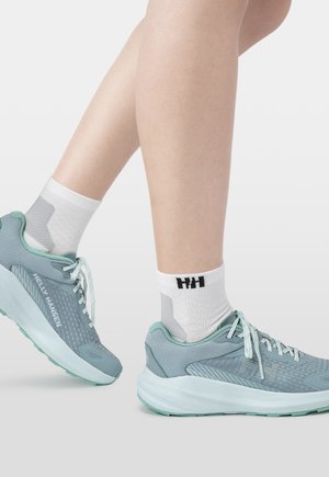 Nogi w białych skarpetkach do kostek i niebiesko-szarych butach sportowych z jasnymi zielonymi akcentami, uniesiona pięta wskazuje na chodzenie lub ruch.