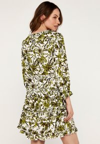 Blumenmuster-Kleid mit grünen Blättern auf weißem Hintergrund, mit Volant-Saum und langen Ärmeln mit Raffung an den Schultern.