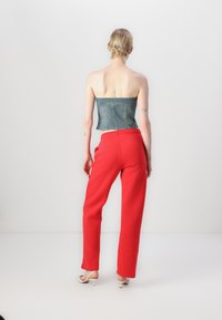 Denim bezramenný top s cropped strihom; v kombinácii s červenými voľnými nohavicami; model má na sebe svetlé sandále; jednoduché, neutrálne pozadie.