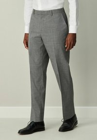 Sivé kárované nohavice z tkaniny, so sklopeným pásom, bočnými vreckami a úzkym strihom, doplnené o čierne spoločenské topánky.