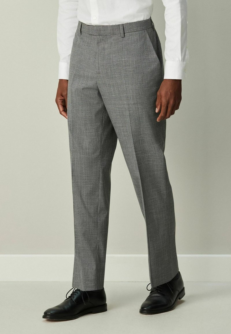 Sivé kárované nohavice z tkaniny, so sklopeným pásom, bočnými vreckami a úzkym strihom, doplnené o čierne spoločenské topánky.