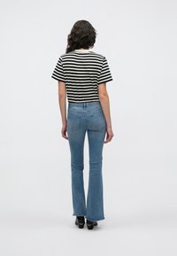 Schwarz-weiß gestreiftes Kurzarmoberteil kombiniert mit hellblauen, ausgestellten Jeans. Das Outfit zeichnet sich durch einen klassischen Schnitt und Denim-Textur aus.