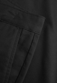 Black fabric detail with a smooth texture, showing a folded hem and stitching lines. The material appears durable and well-structured.
