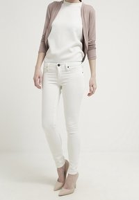 Białe dopasowane dżinsy w połączeniu z fakturowaną białą bluzką i jasnoróżowym kardiganem. Obuwie to cieliste szpilki.