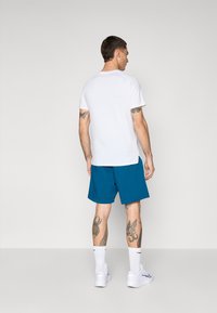 T-shirt branca de manga curta combinada com calções em tom teal. Os calções têm um corte descontraído e o visual é complementado com ténis brancos e meias até ao tornozelo.
