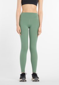 Leggings de talle alto y ajuste ceñido en un tono verde apagado, fabricados con material elástico, con bolsillos laterales y textura suave.